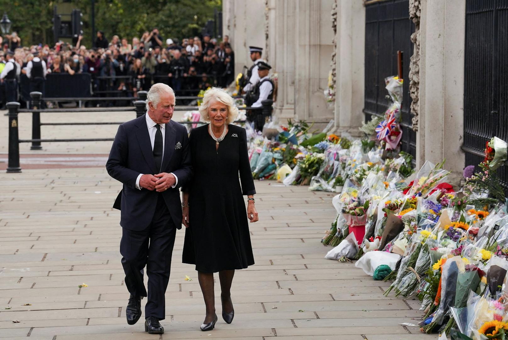König Charles und Camilla schreiten gemeinsam den Zaun des Buckingham-Palastes entlang, wo unzählige Blumensträusse niedergelegt wurden.