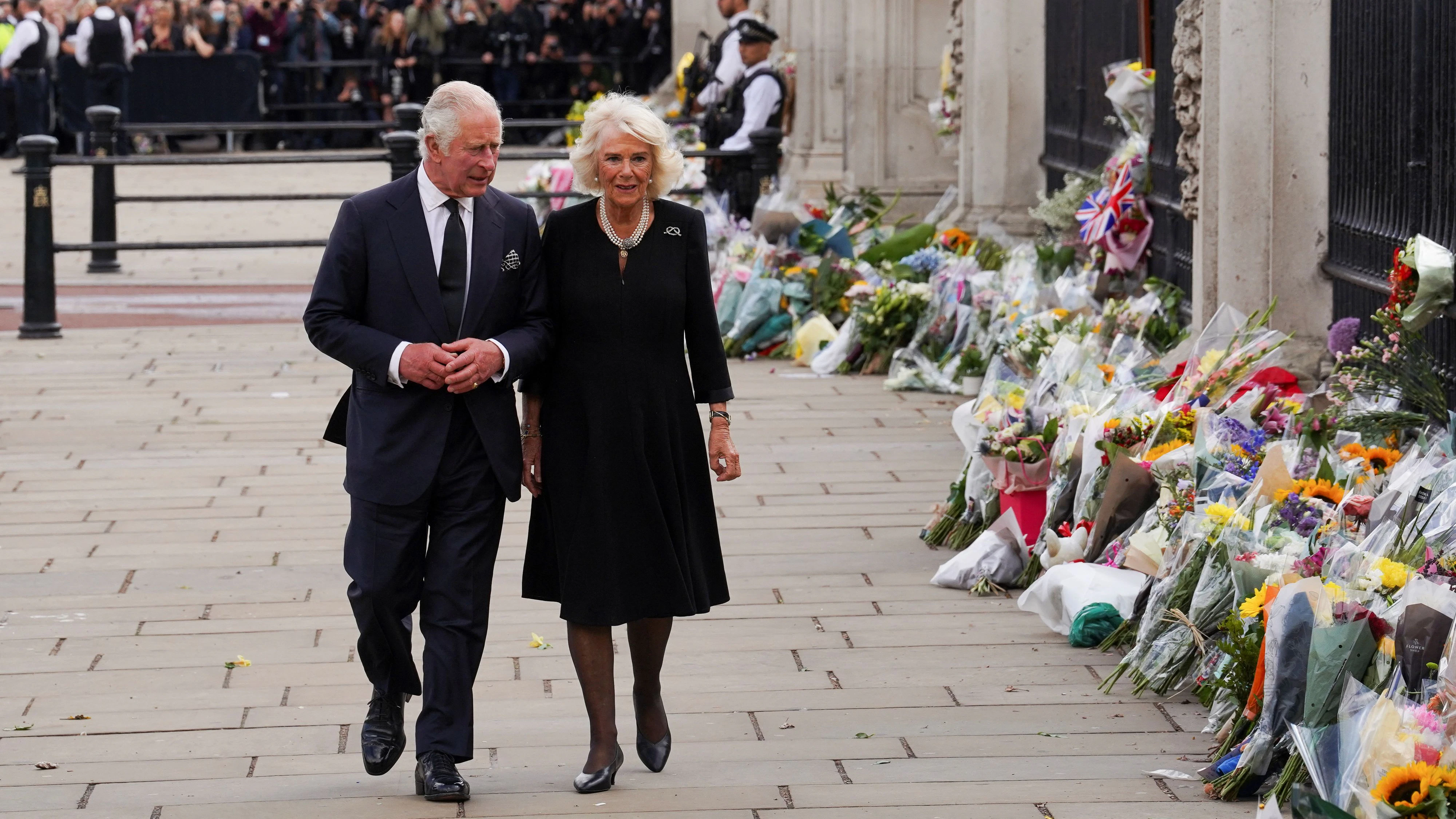 König Charles und Camilla schreiten gemeinsam den Zaun des Buckingham-Palastes entlang, wo unzählige Blumensträusse niedergelegt wurden.