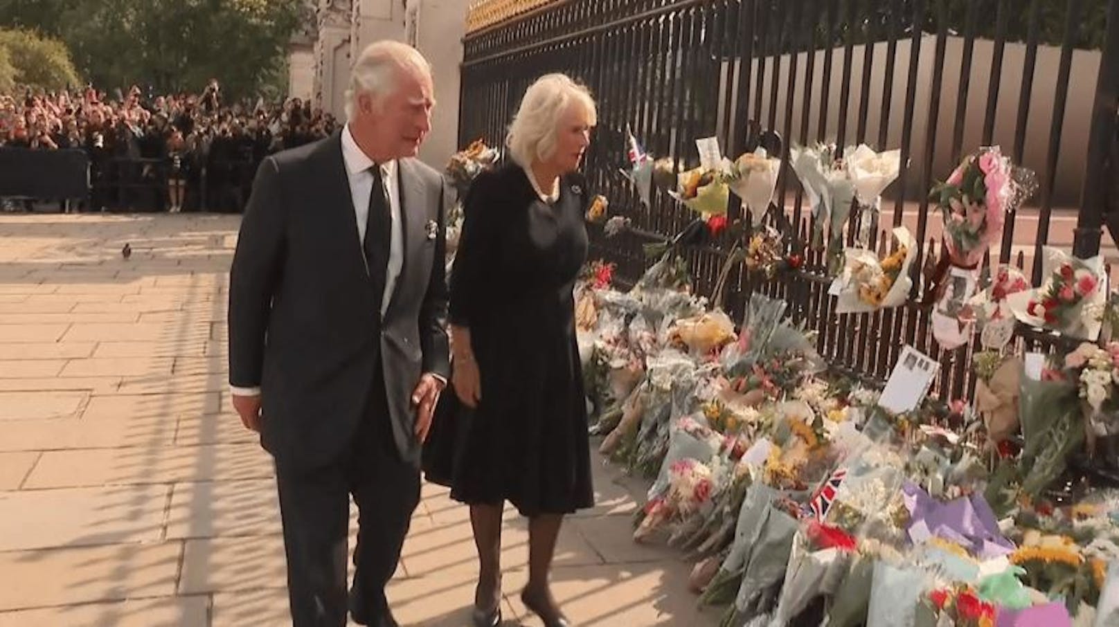 König Charles und Camilla schreiten gemeinsam den Zaun des Buckingham-Palastes entlang, wo unzählige Blumensträuße niedergelegt wurden.