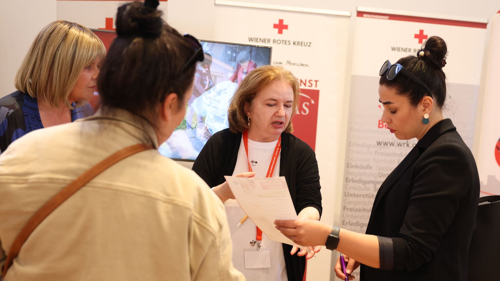 Gabriela U. (57) in ihrem neuen Job beim Roten Kreuz, umringt von Interessentinnen auf der Jobmesse.