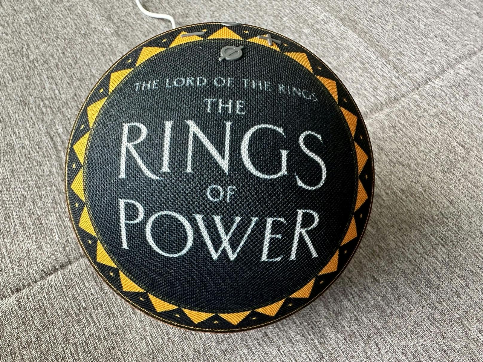 ...findet sich in weißen Lettern der Schriftzug "The Lord of the Rings The Rings of Power", umrandet von einem gelb-goldenen Kreis aus Dreiecken und Punkten.