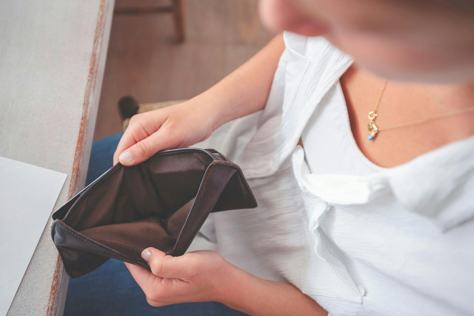 Eine Frau blickt verzweifelt in ihre leere Geldbörse. Symbolbild.
