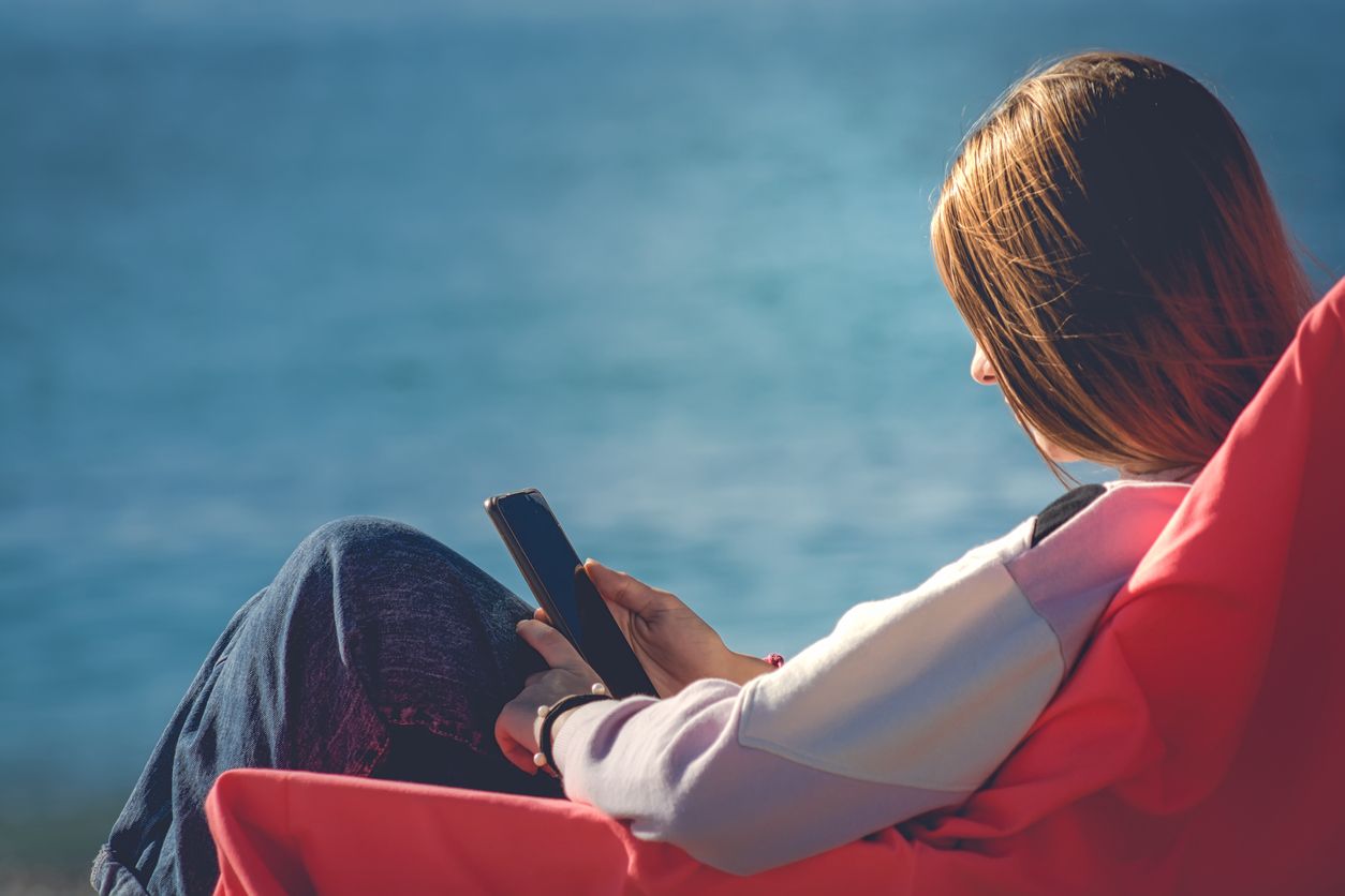 girl sunbathing on a red sun lounger on the beach using her smart phone