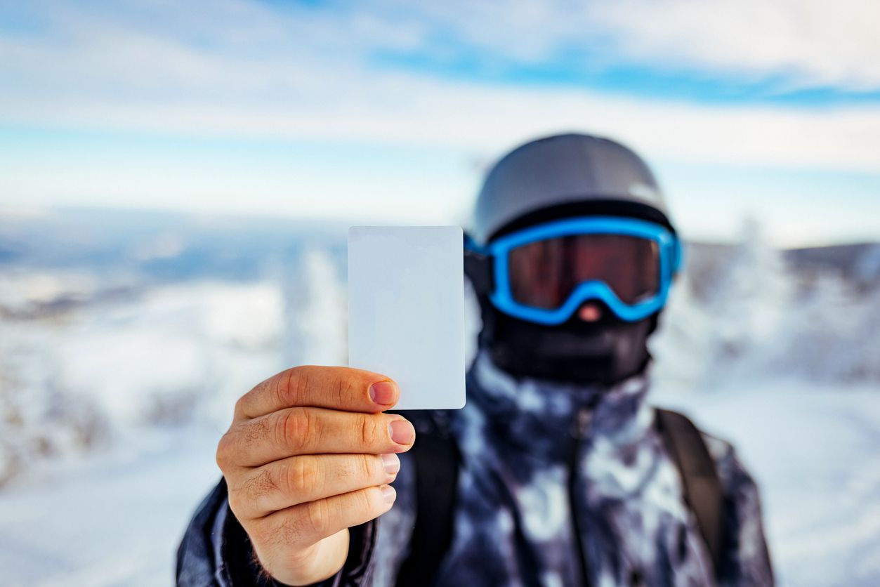 Man with winter sport equipment looking at camera. One hand  is showing a blank lift pass. Concept to illustrate ski admission fee