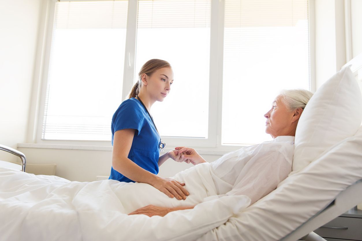medicine, age, support, health care and people concept - doctor or nurse visiting and cheering senior woman lying in bed at hospital ward