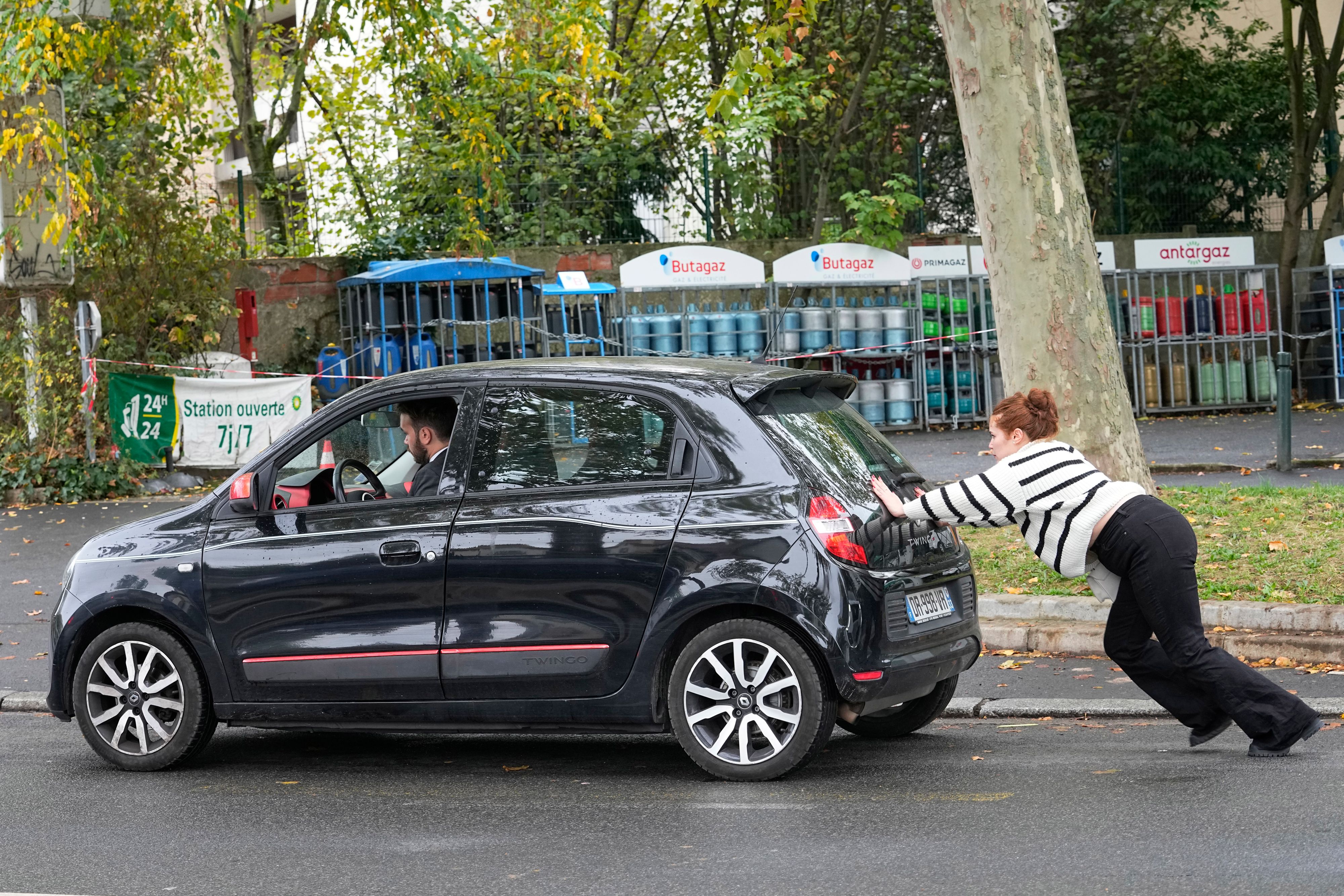 Ein Auto wird in Paris zu einer  Tankstelle geschoben. Einer der  zwei hat dabei den besseren Job.