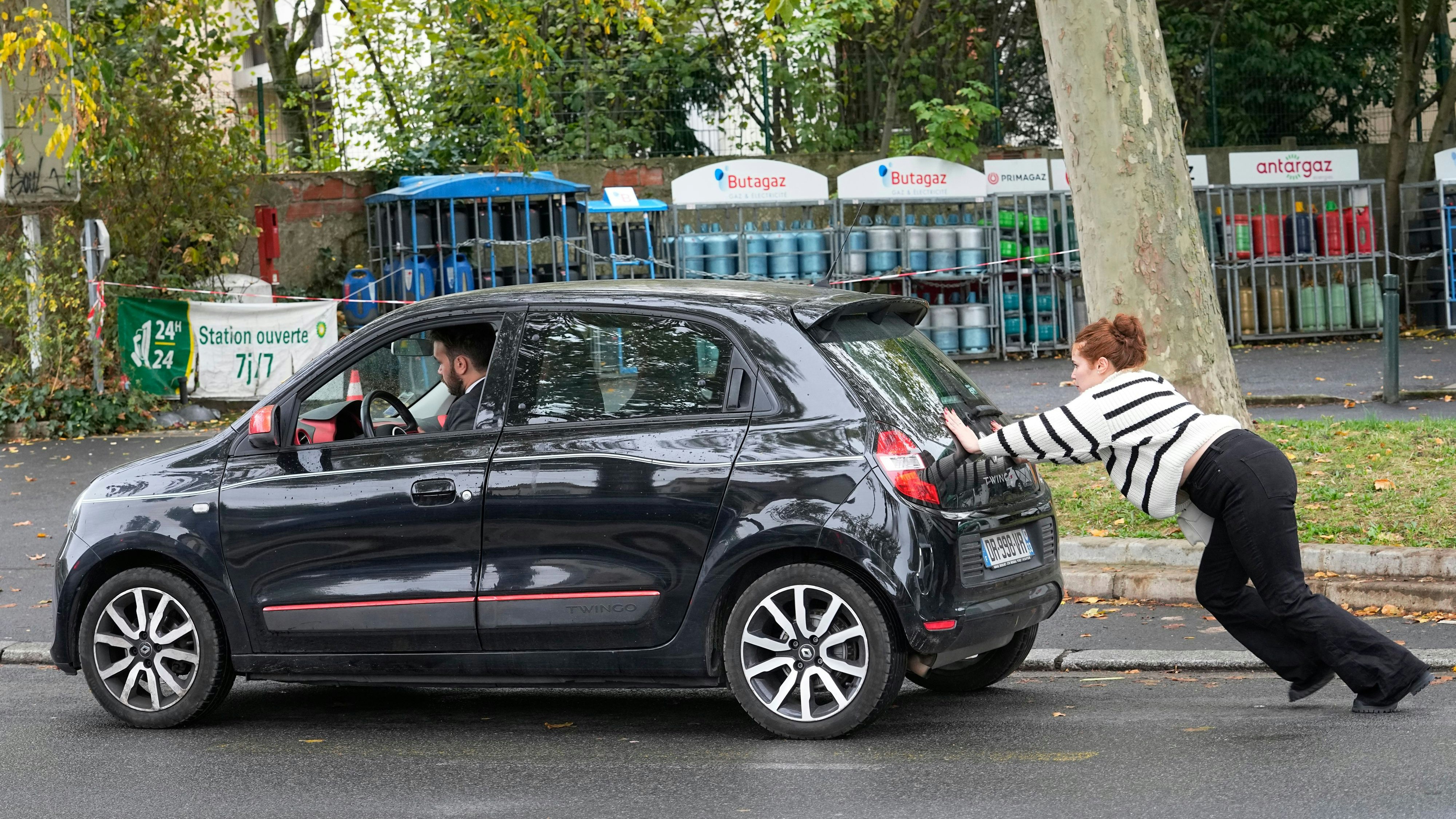Ein Auto wird in Paris zu einer  Tankstelle geschoben. Einer der  zwei hat dabei den besseren Job.
