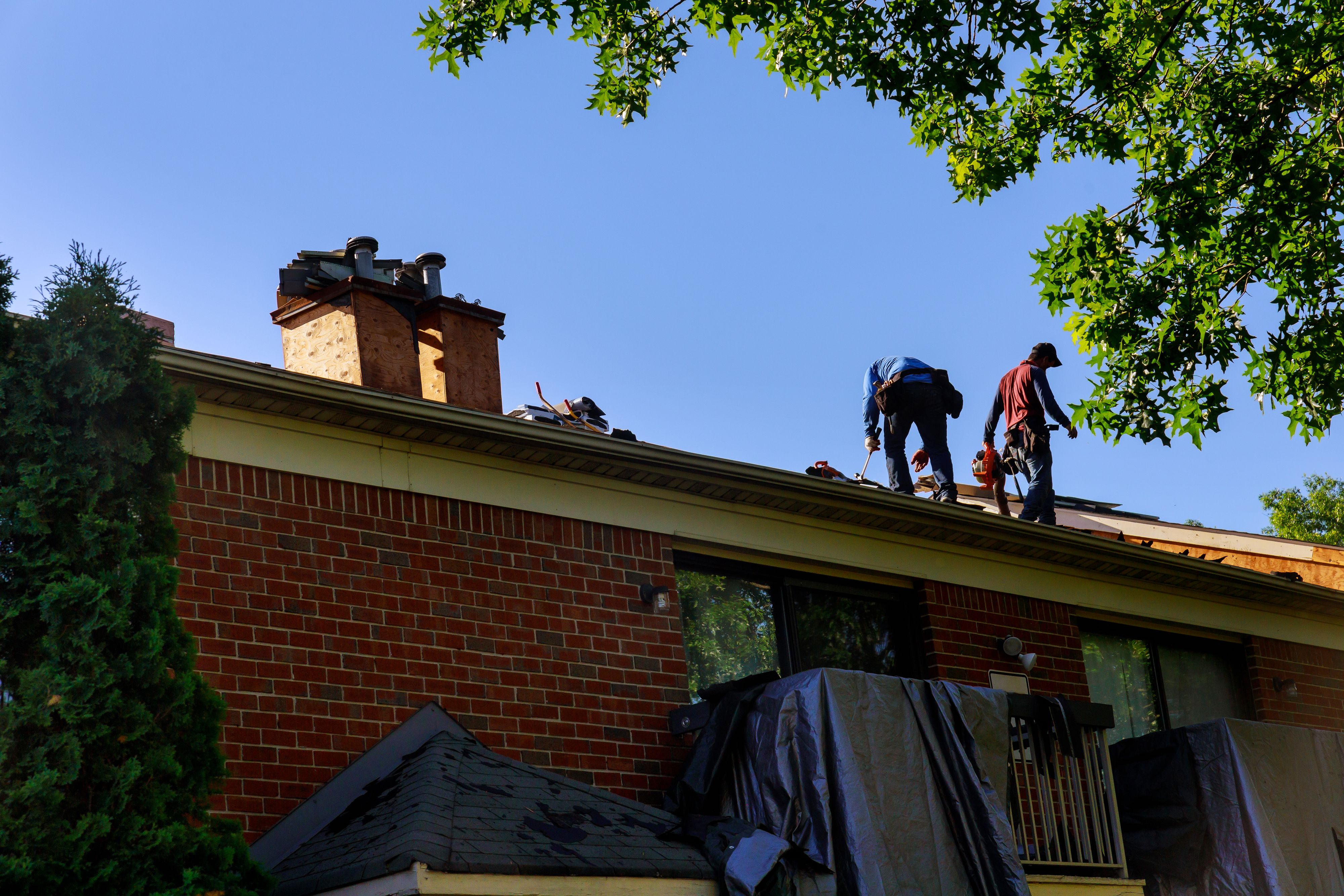 A roofer nailing shingles with air gun, replacing roof cover protection being applied, apartment development