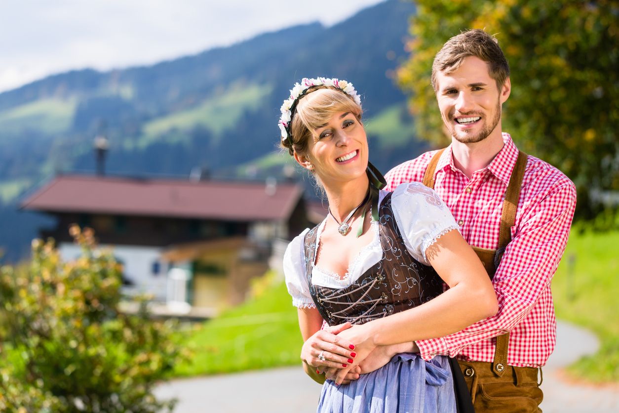 Couple in Tracht standing on meadow in alp mountains, a cable car is running in the background