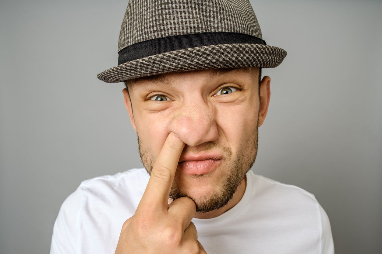 Man picking his nose. The emotional portrait of man in hat and blank t-shirt. Gray background