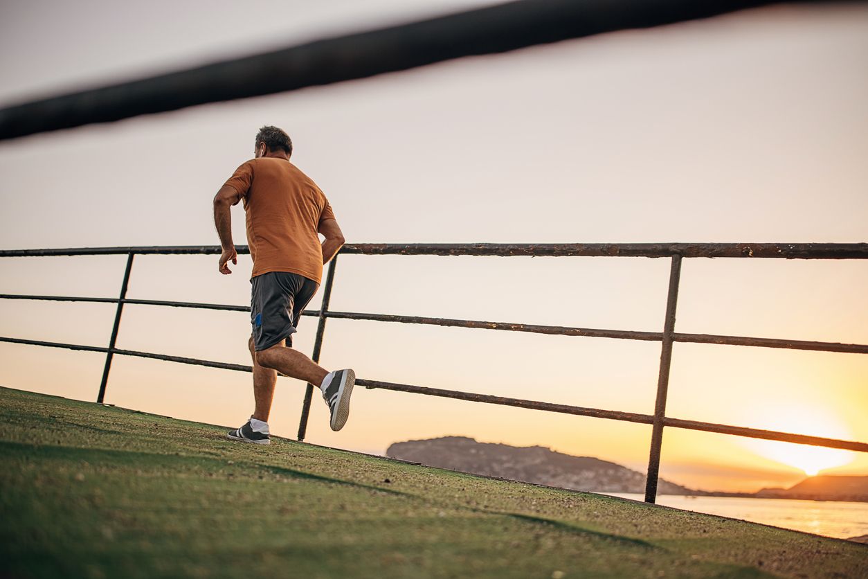 One man, senior male jogging on pier by the sea alone in sunset.