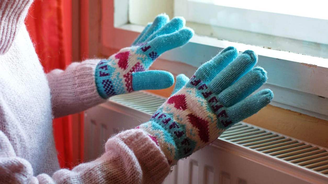 A woman hands in wool gloves warms near the heater
