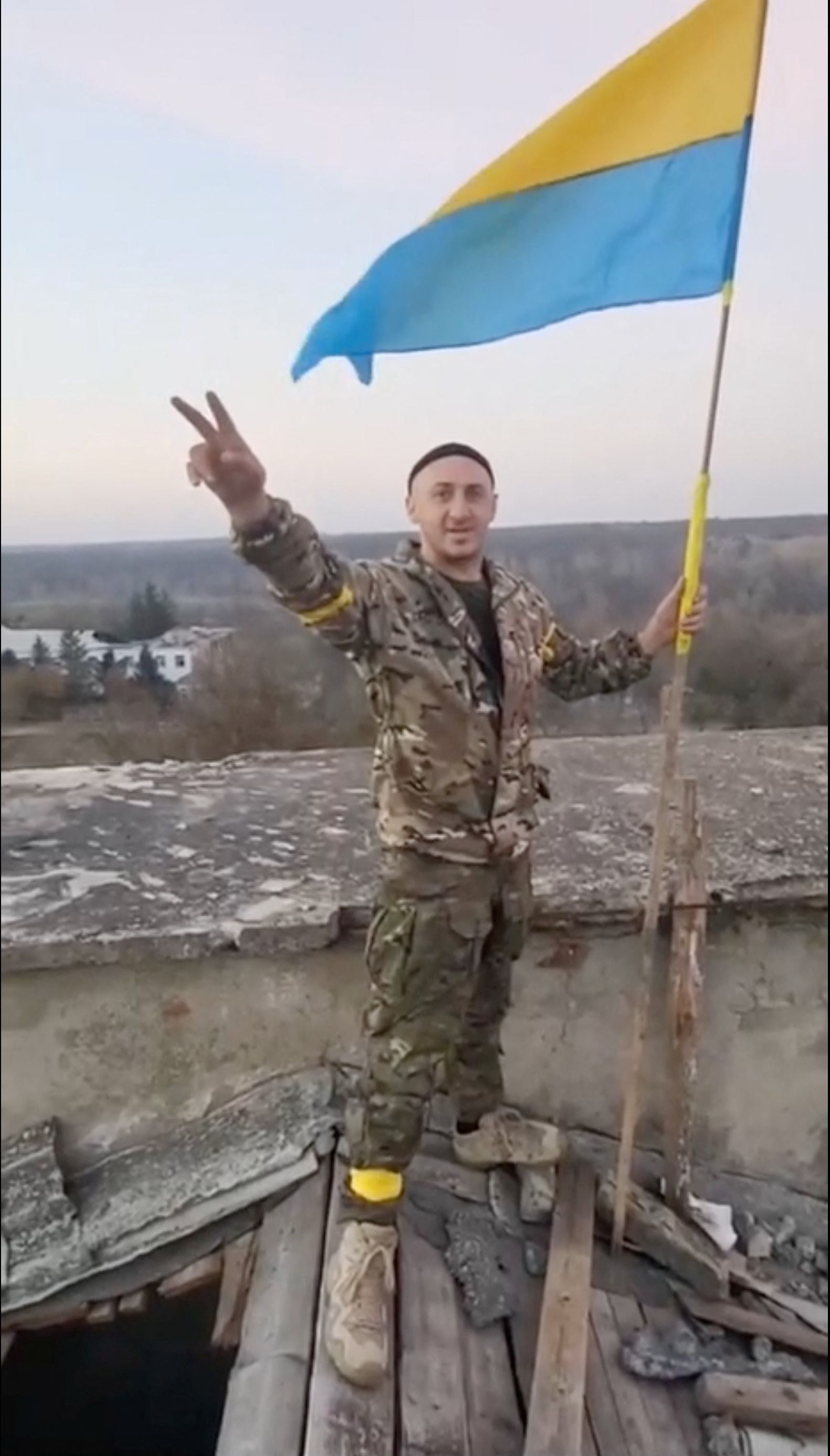Ein Mann in Militärkleidung bei einer Siegesgeste neben einer ukrainischen Flagge in Kalynivske in der Region Cherson am 9. November 2022.