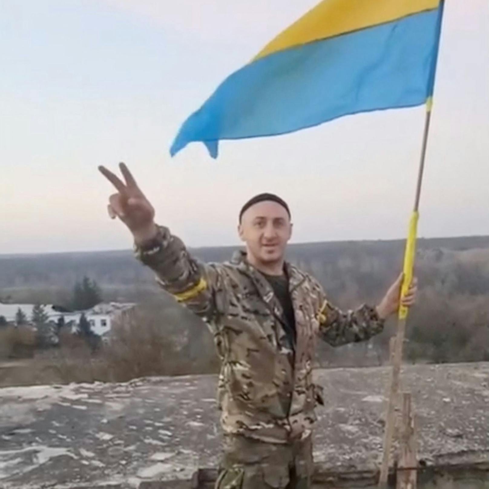 Ein Mann in Militärkleidung bei einer Siegesgeste neben einer ukrainischen Flagge in Kalynivske in der Region Cherson am 9. November 2022.
