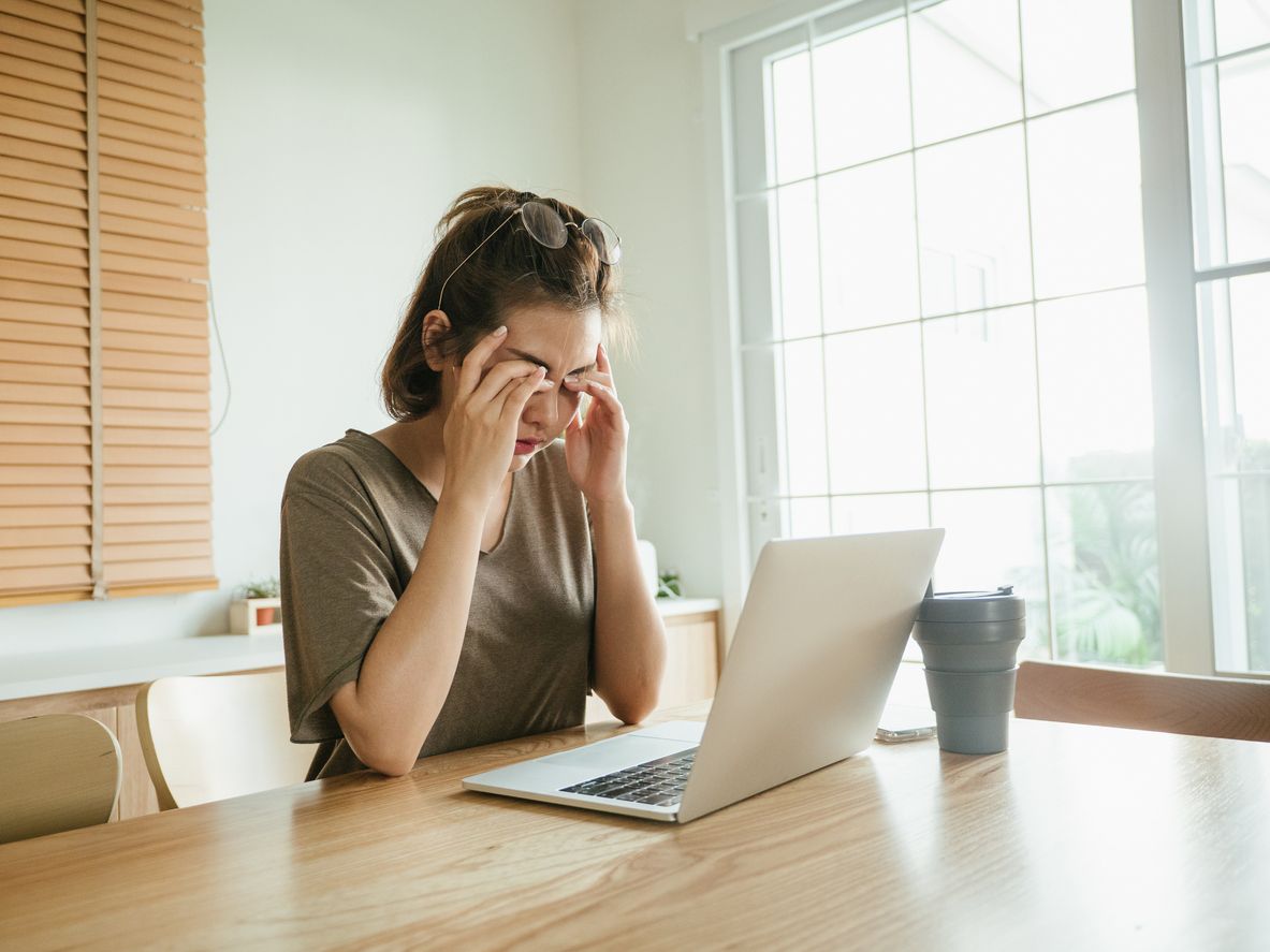 Exhausted freelancer woman rubbing her eyes while working on laptop at home.