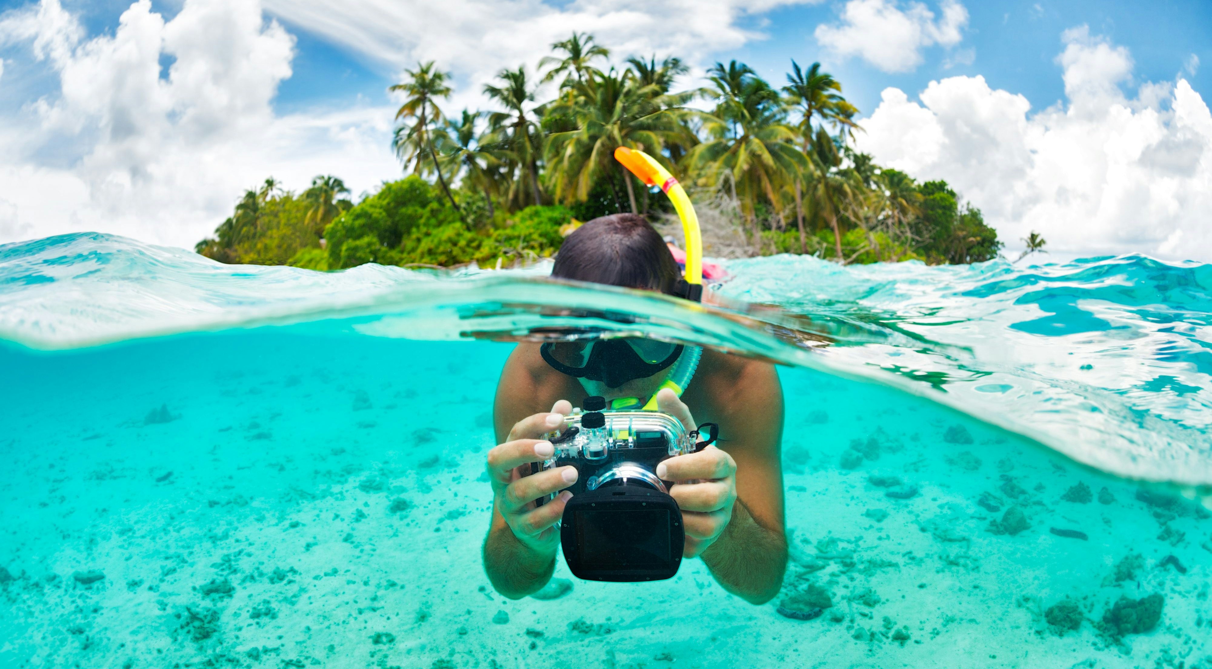Male diver snorkeling and filming underwater surroundings.