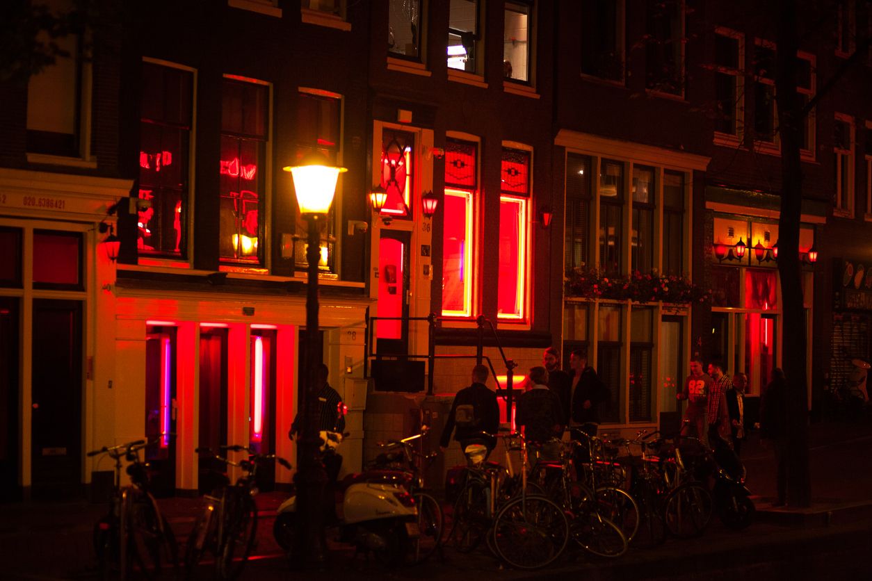 Amsterdam, The Netherlands - October 2, 2015: Men are walking along sex cabins of prostitutes at canal in Wallen in Amsterdam at night. Bicycles are parked at canal. Windows are red illuminated.