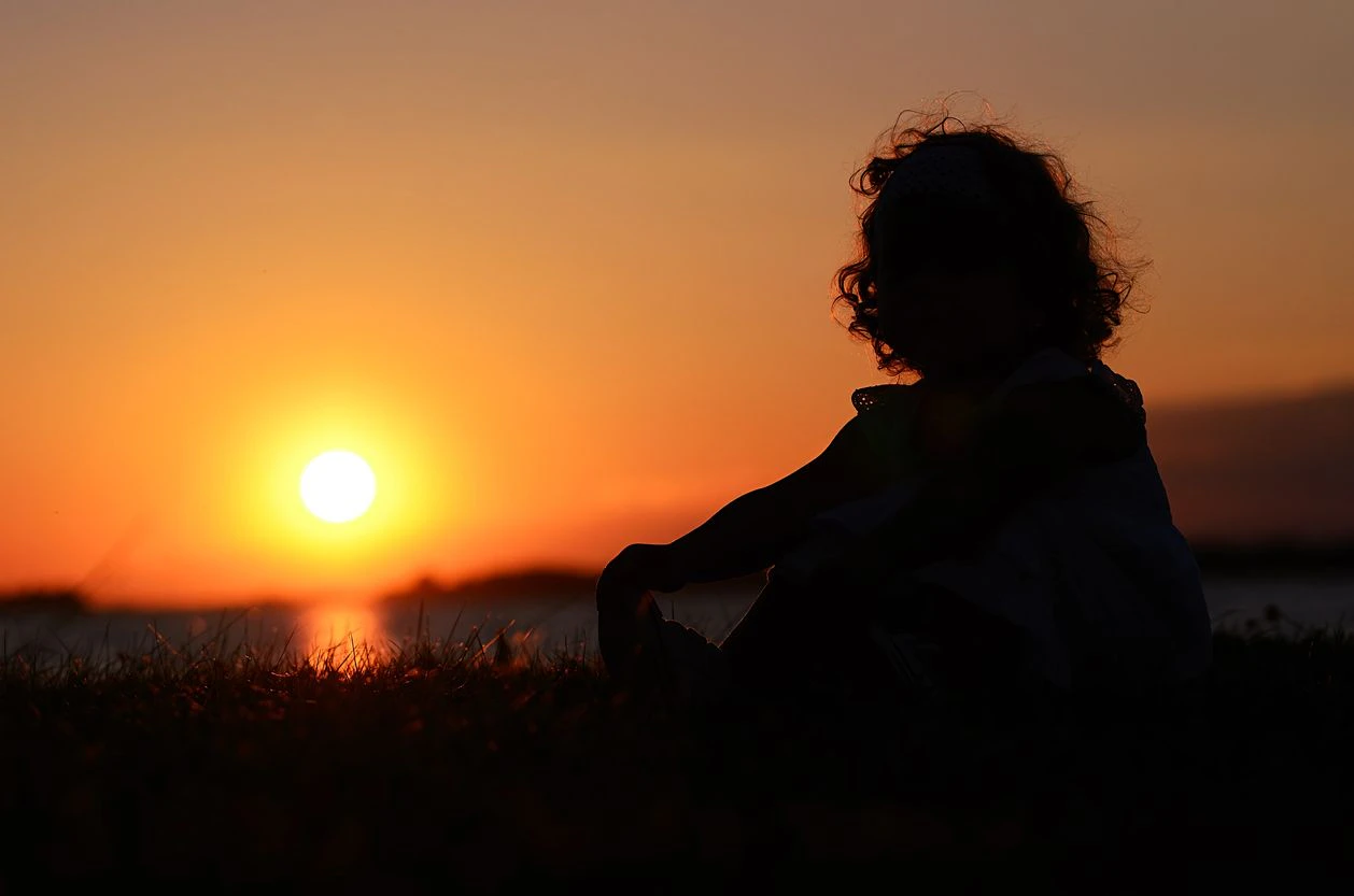 Silhouette photo of relaxing young child at the lake in sunset