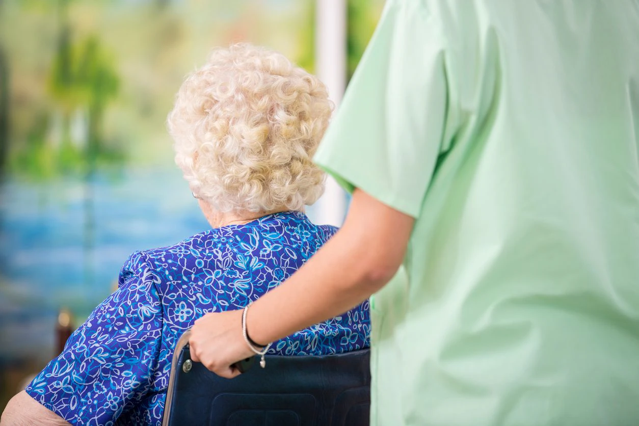 Latin descent home healthcare nurse assists her 100-year old patient during home visit in nursing home setting.  Rear view.