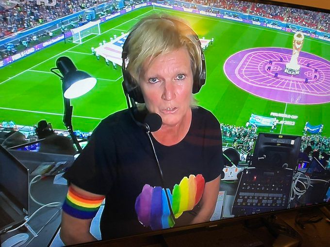 Claudia Neumann grüßt mit Regenbogen-Schleife und buntem Shirt aus dem Stadion.