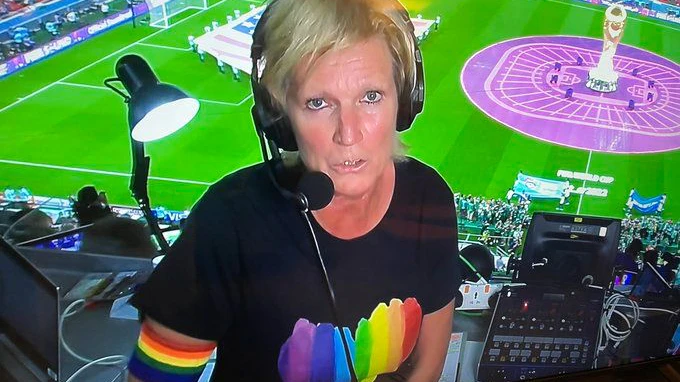 Claudia Neumann grüßt mit Regenbogen-Schleife und buntem Shirt aus dem Stadion.