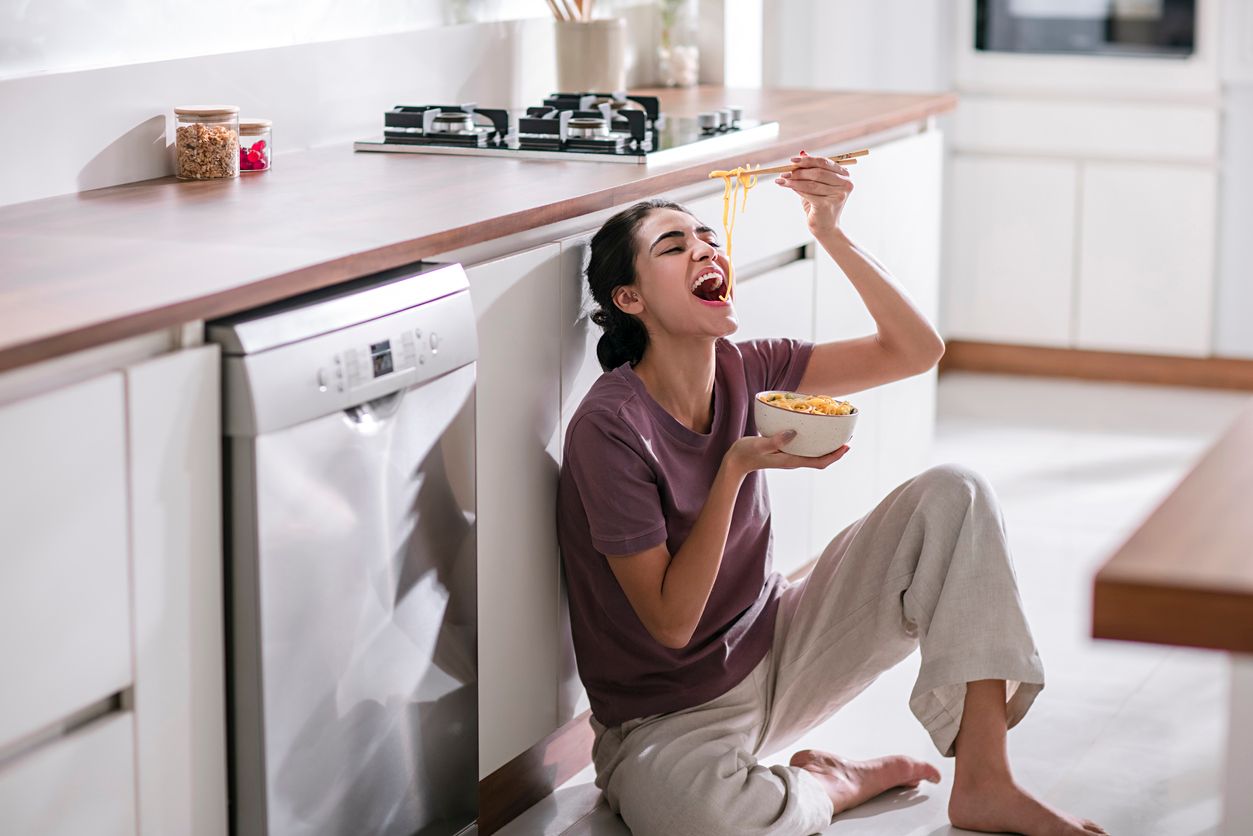 Young woman eating noodles in the kitchen