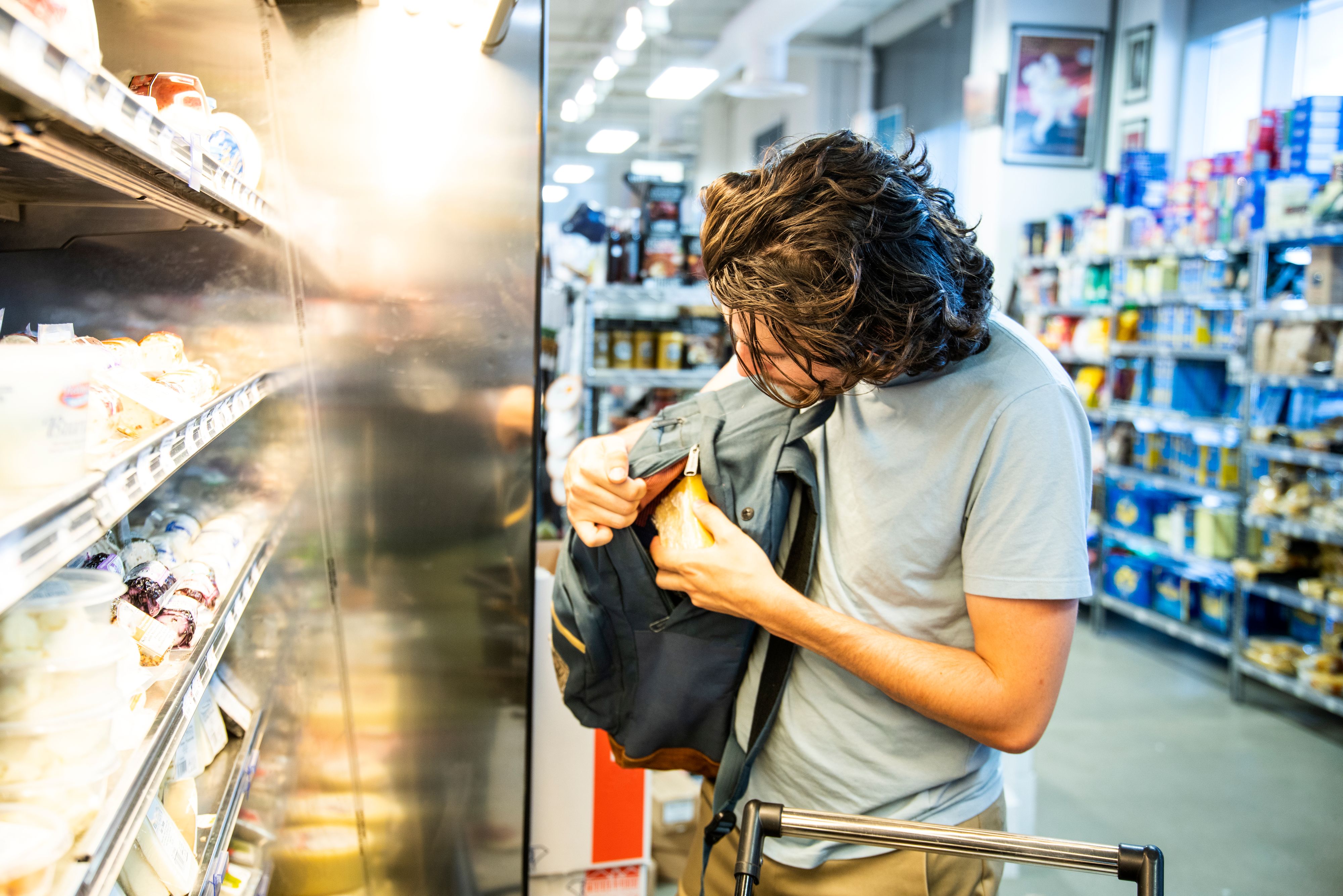 A male shoplifter stealing some expensive gourmet cheese in a specialty supermarket