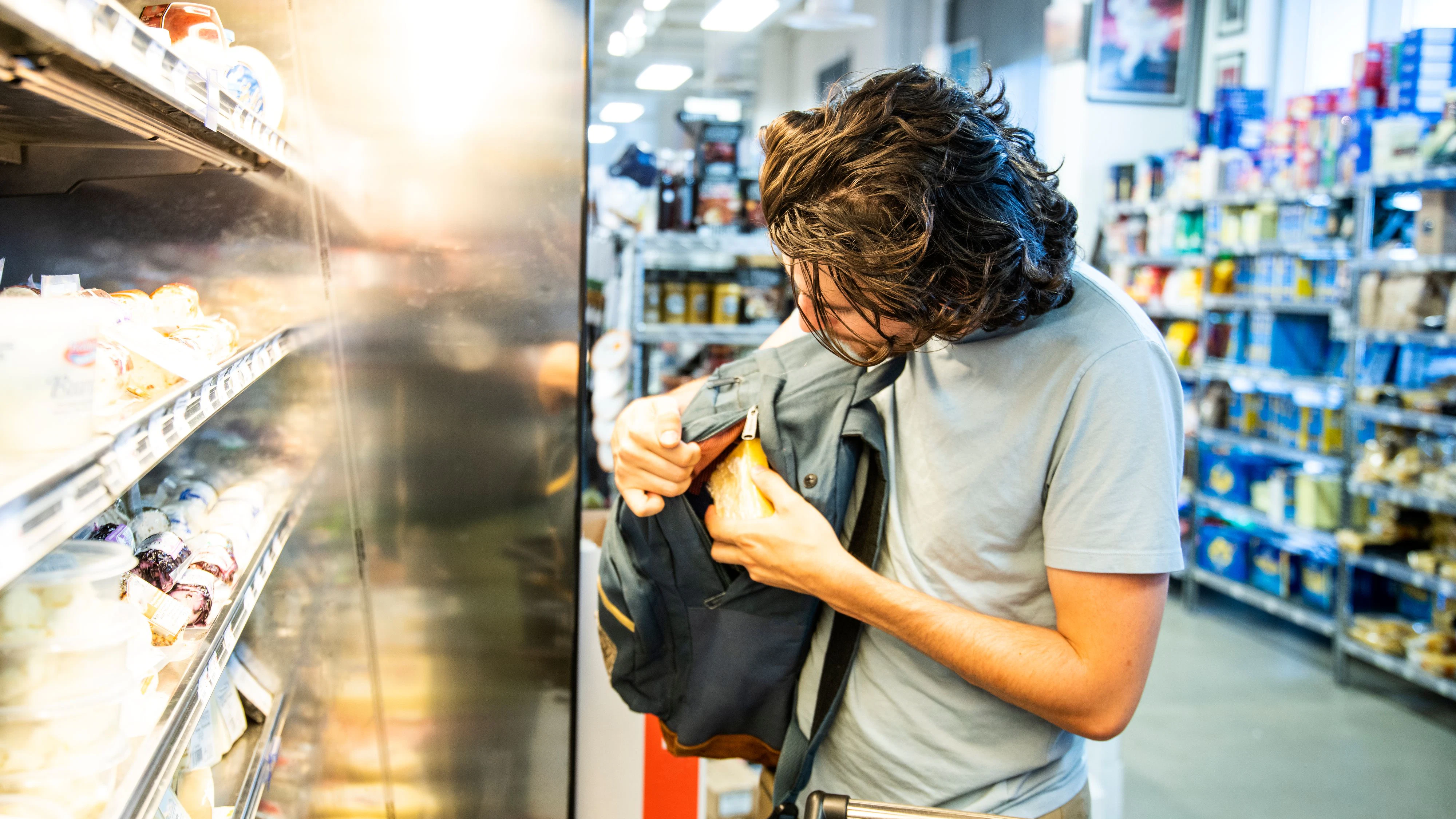 A male shoplifter stealing some expensive gourmet cheese in a specialty supermarket