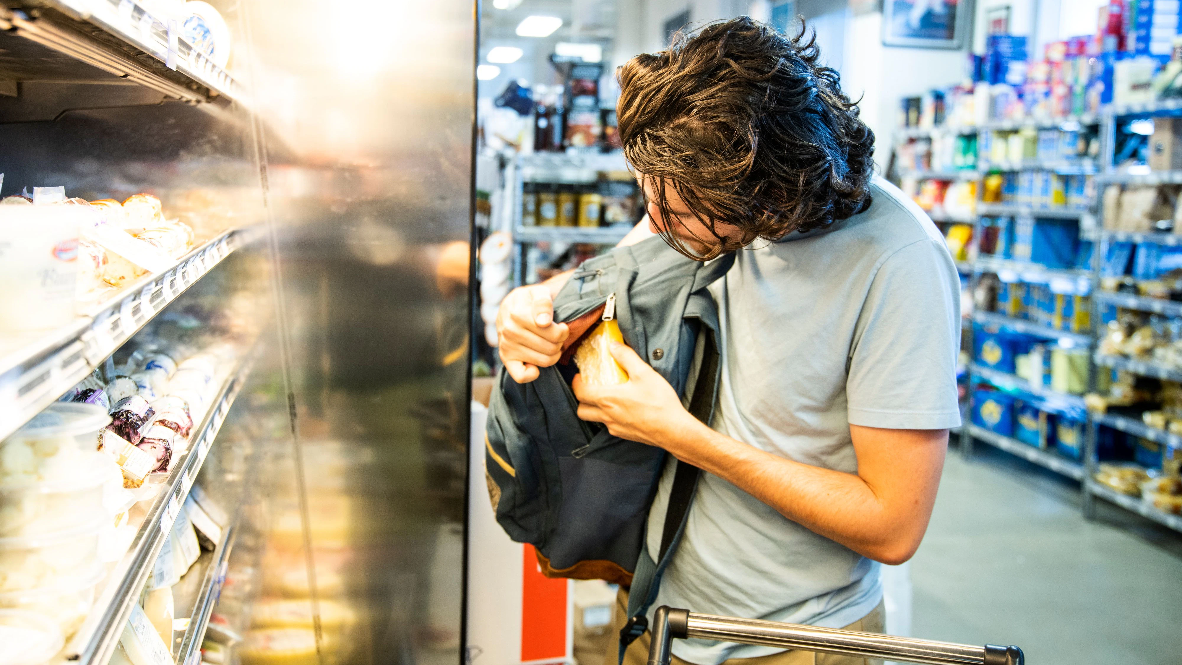 A male shoplifter stealing some expensive gourmet cheese in a specialty supermarket