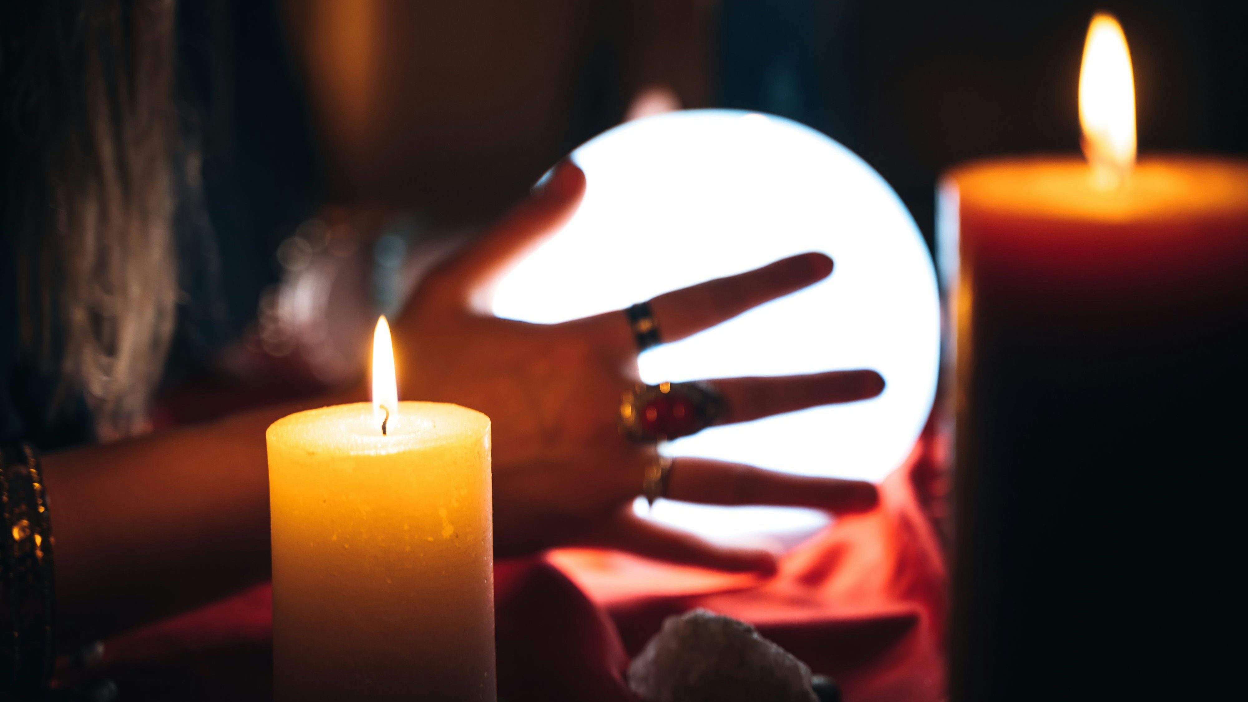 Young female fortune teller is looking into glowing crystal sphere