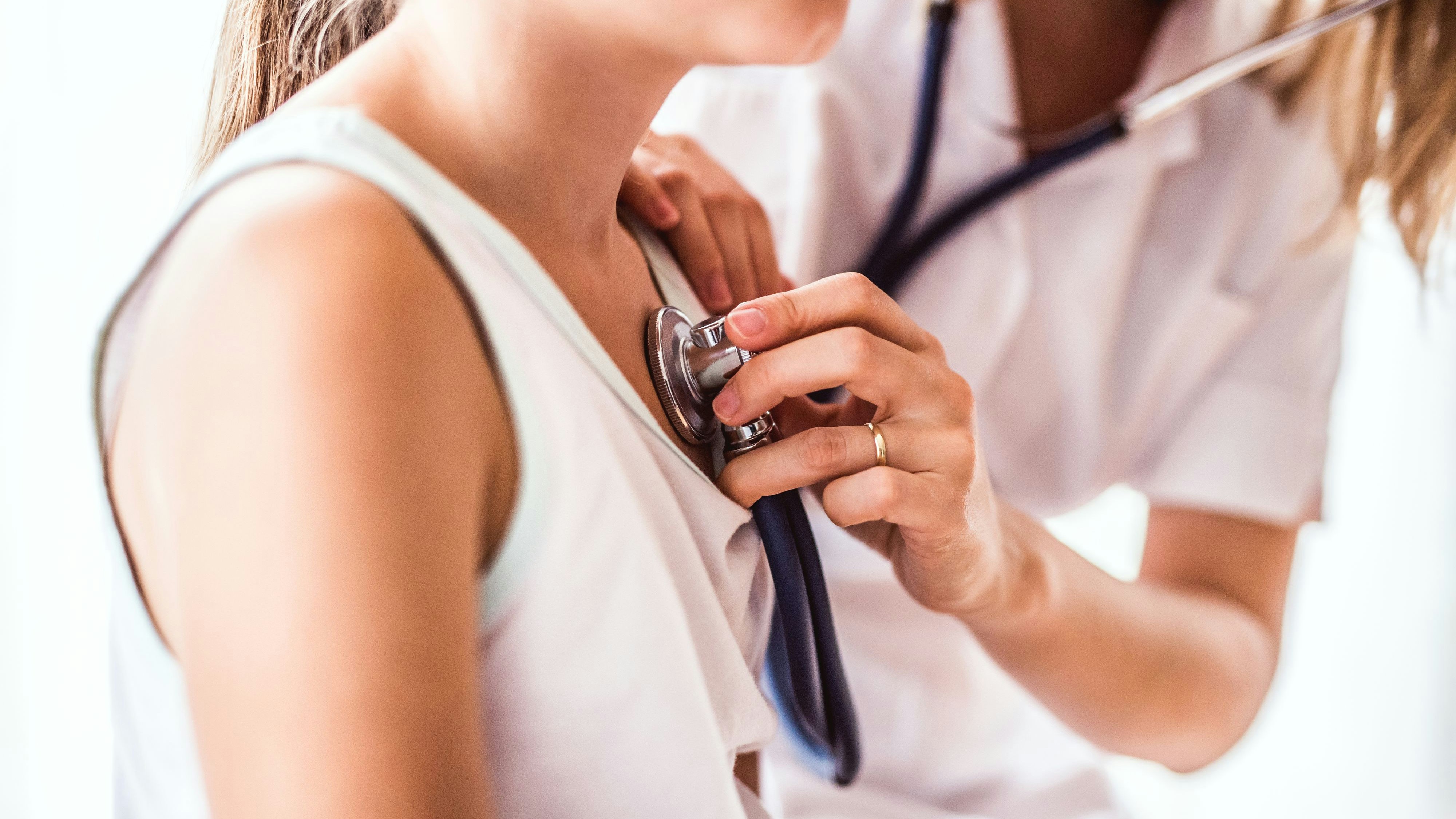 Unrecognizable young female doctor examining a small girl with stethoscope in her office. Close up.