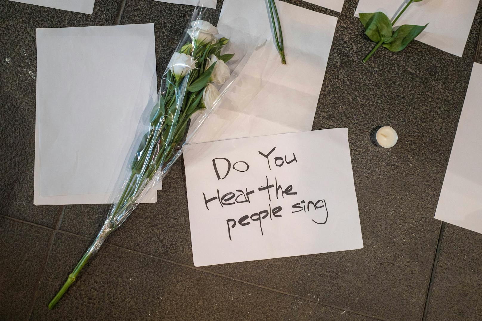 Gedenkblumen und leere Zettel sind während der Demonstration neben einer Kerze zu sehen. Weiße, leere Zettel werden als Symbol gegen die omnipräsente Zensur in China während der Proteste verwendet.