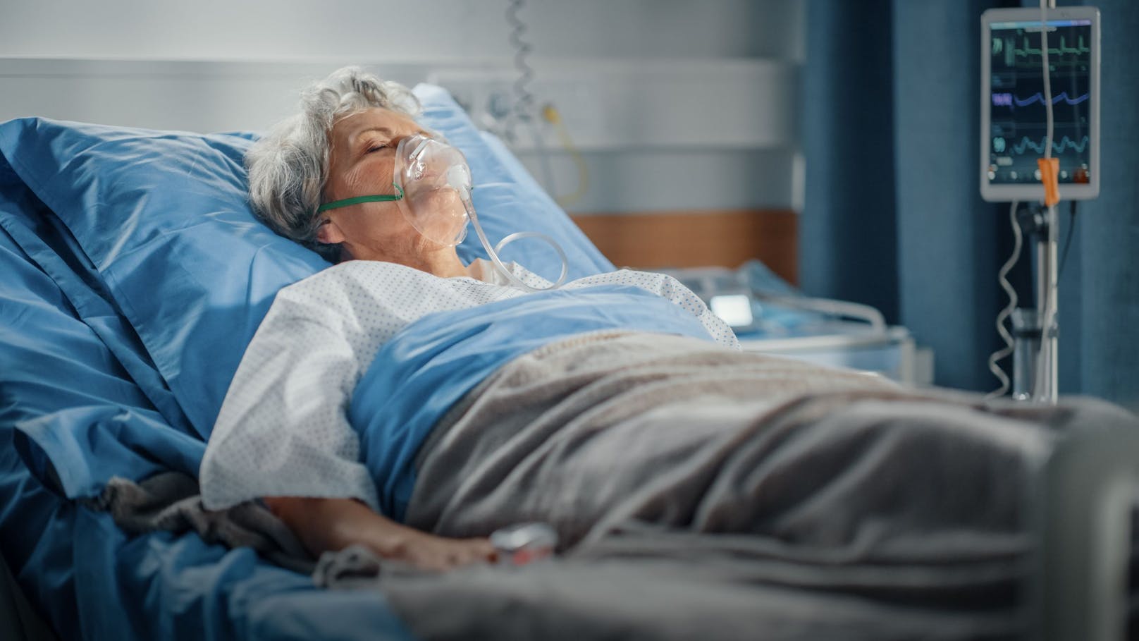 Eine ältere Frau mit angelegter Sauerstoffmaske in einem Krankenbett. Symbolbild