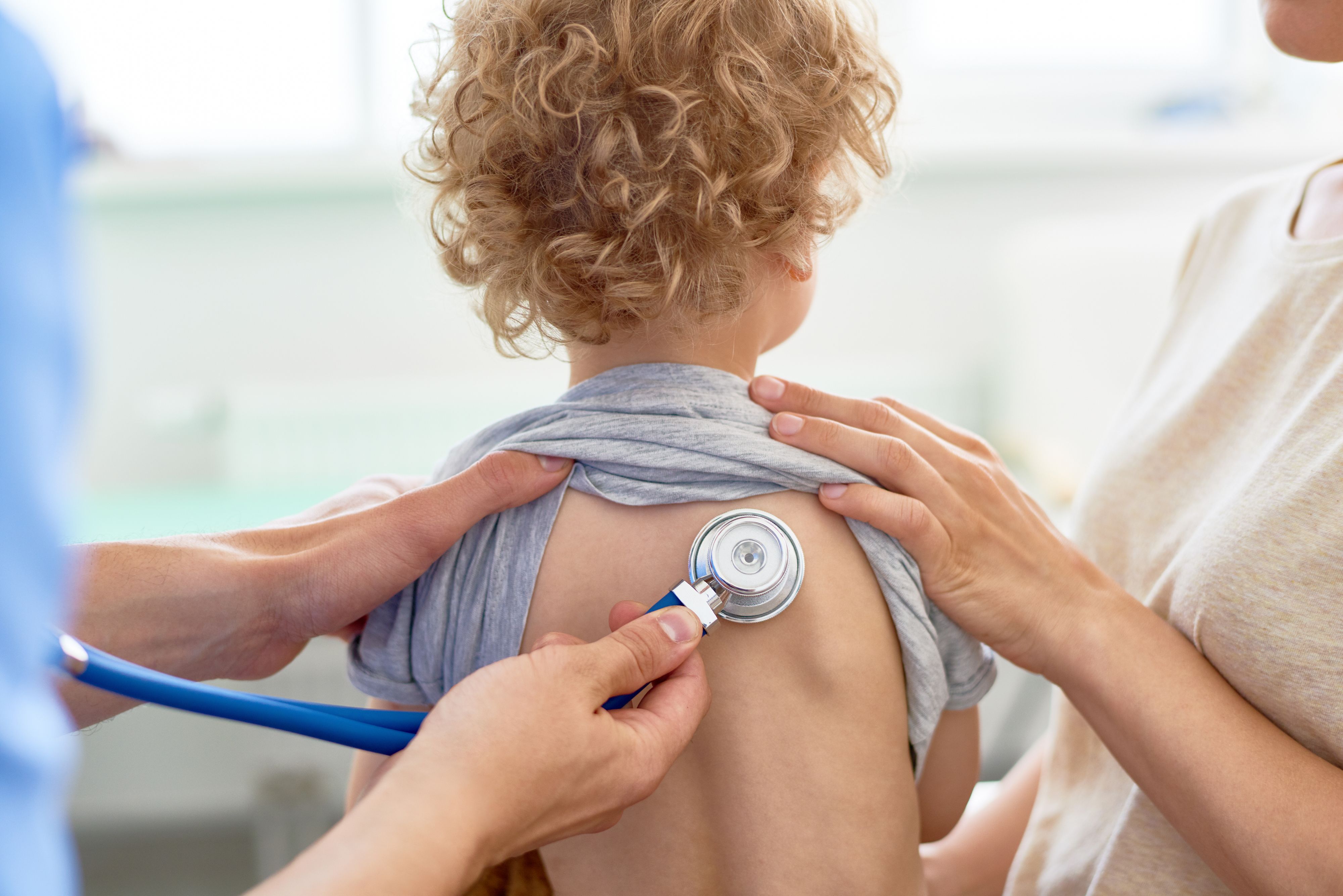 Unrecognizable male pediatrician examining curly little patient with help of stethoscope, blurred background