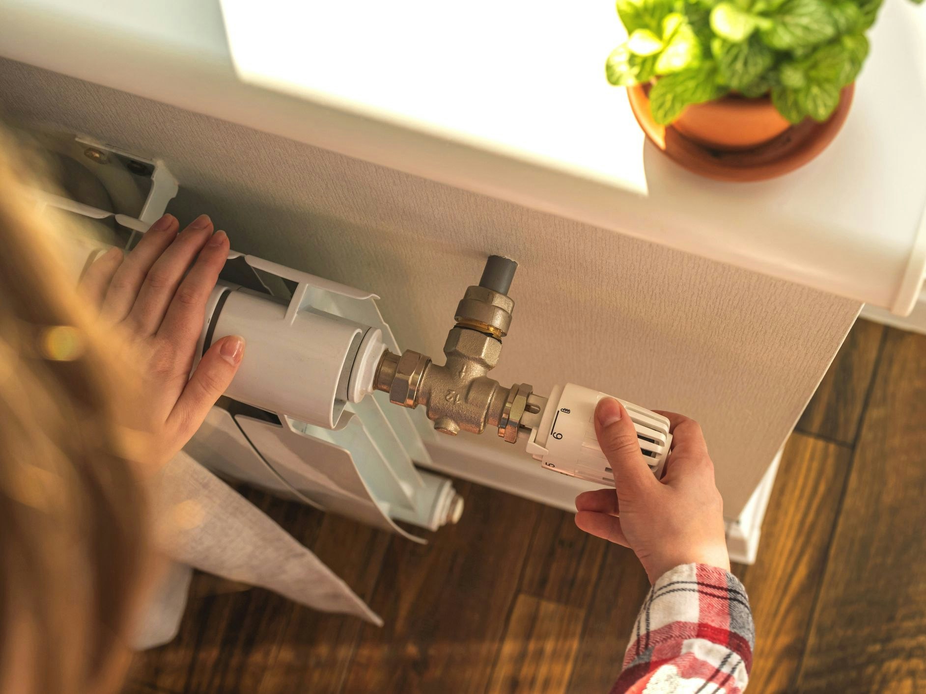 Woman adjusting the temperature on valve of a radiator at home, modern interior background