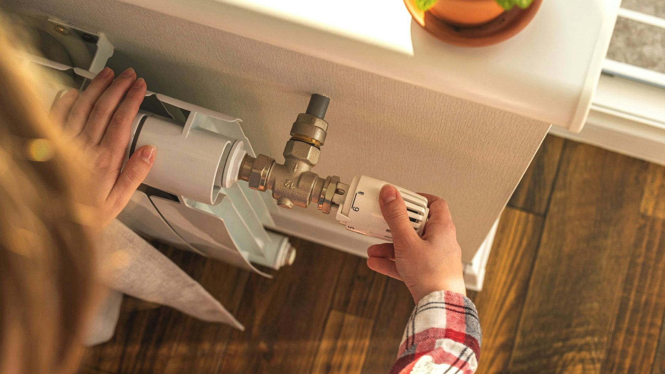 Woman adjusting the temperature on valve of a radiator at home, modern interior background