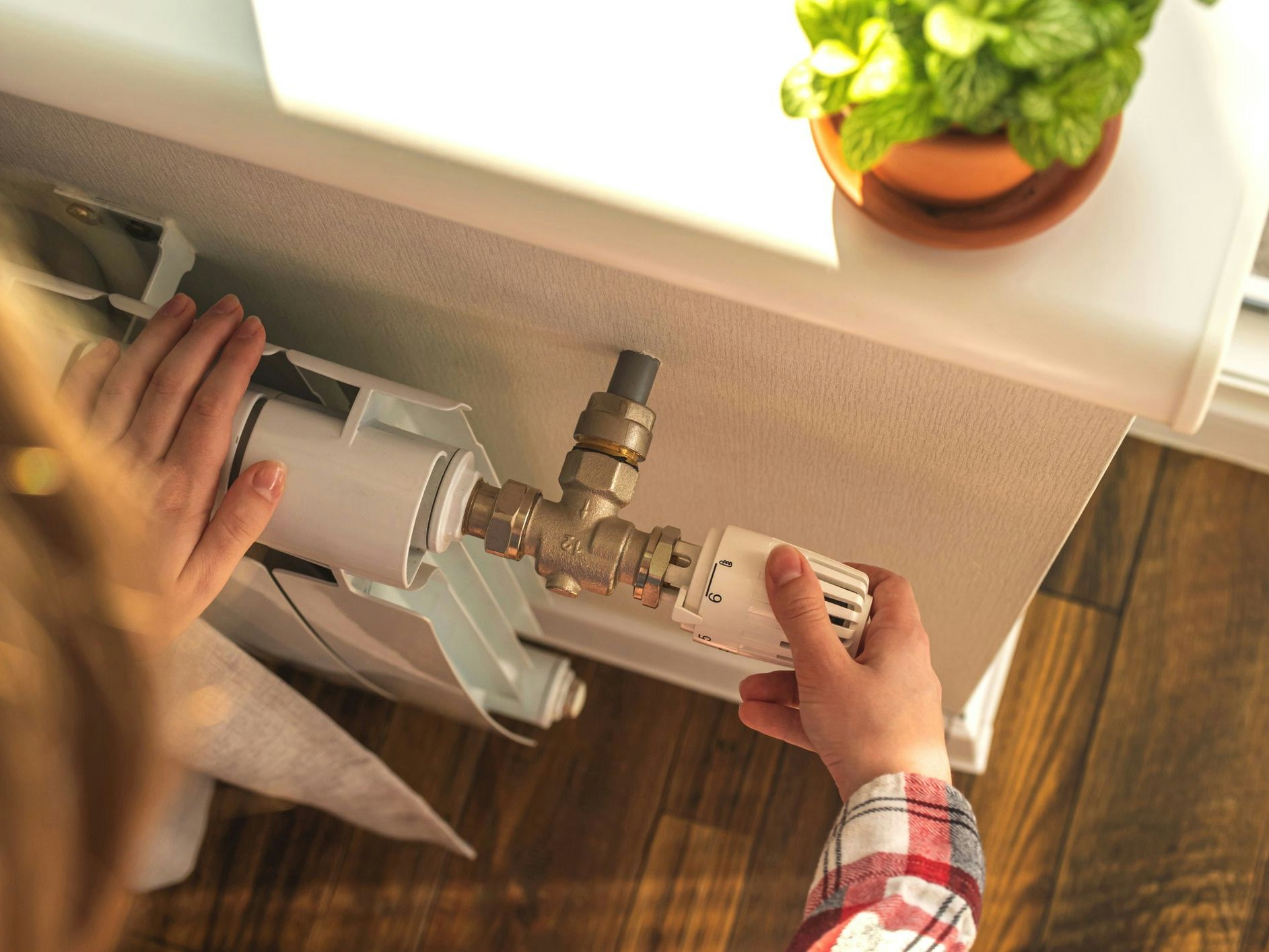 Woman adjusting the temperature on valve of a radiator at home, modern interior background