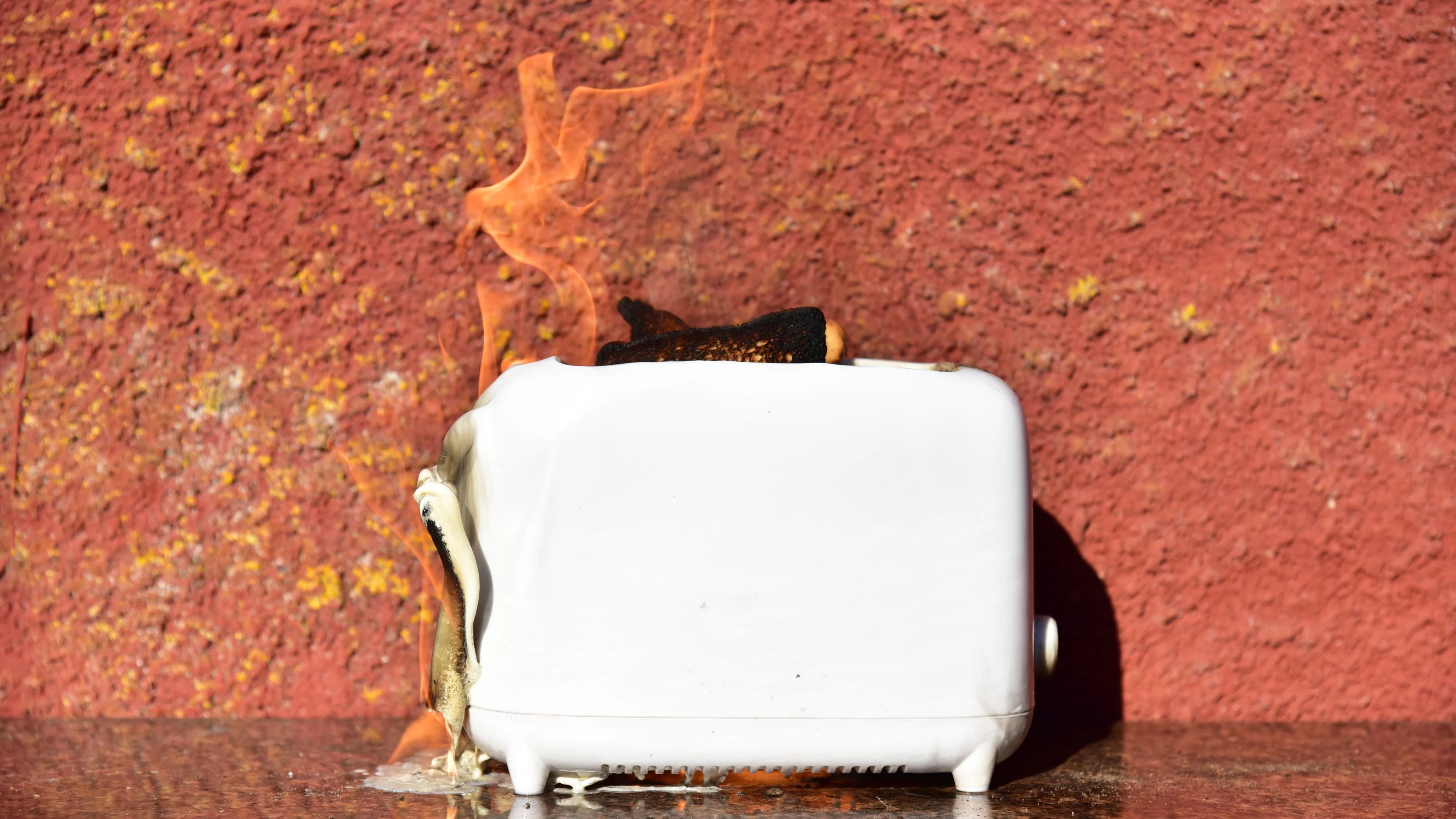 Burning toaster. Toaster with toast caught on fire over table.