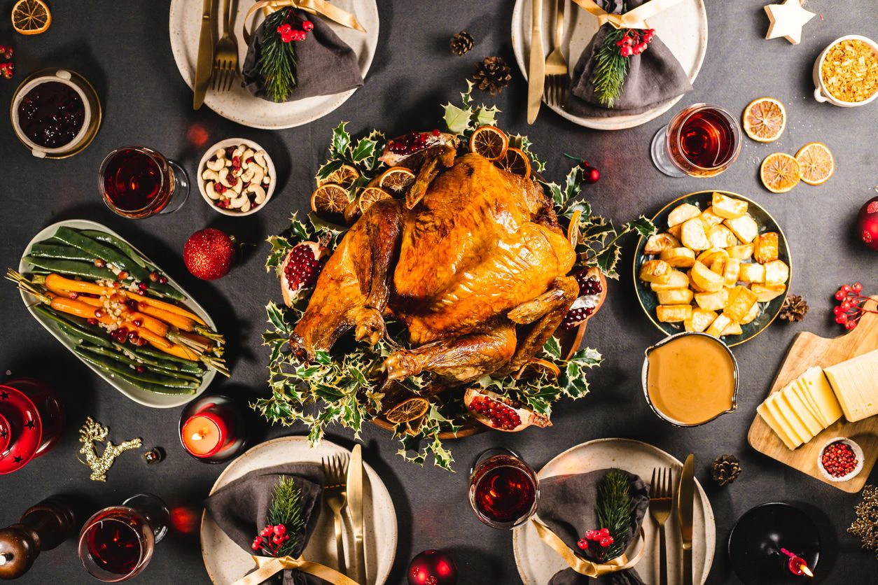 Directly above view of a delicious Christmas meal with roasted Turkey, carrots, cashews, pomegranates, dried oranges and red wine on the dinner table.