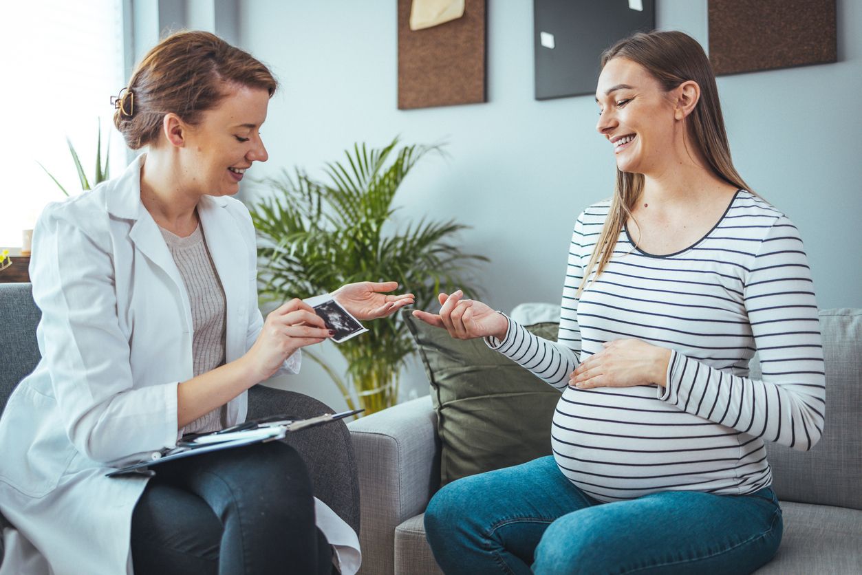 Young  woman smiles while looking at her baby's ultrasound image. She is meeting with a home healthcare nurse. Pregnant woman and doctor looking at her baby ultrasound picture