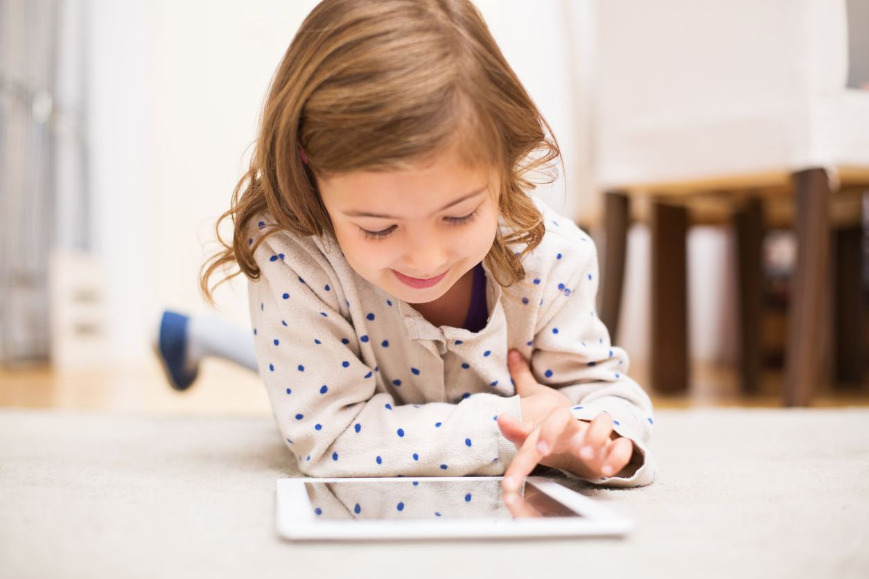 Image of little girl lying on floor learning using digital tablet at home
