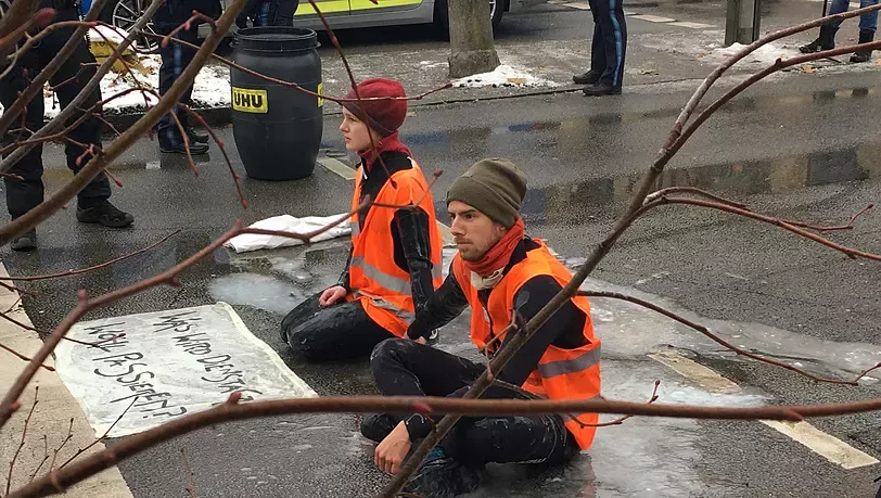 Zwei Aktivisten sitzen auf einer Straße – mit Kleber überschüttet.