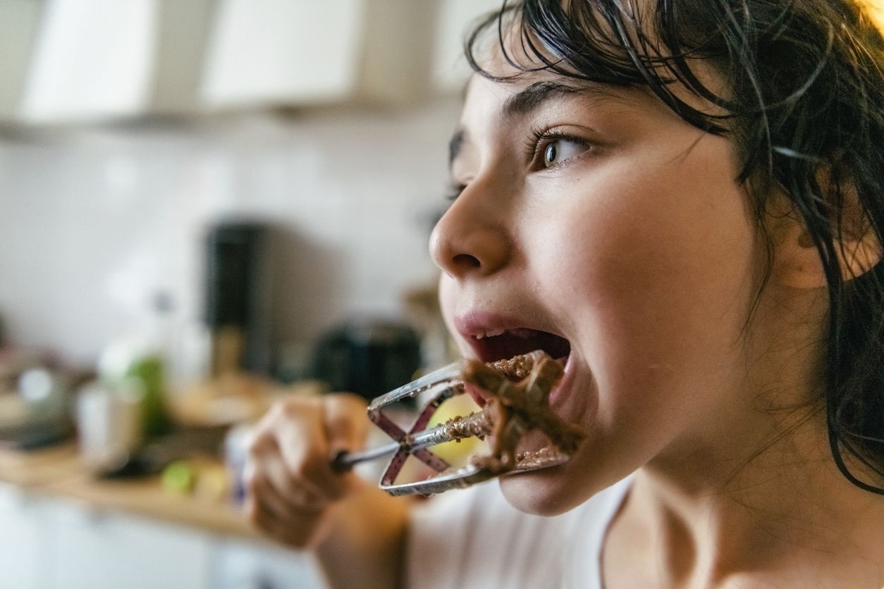portrait of little girl licking blender with chocolate dough