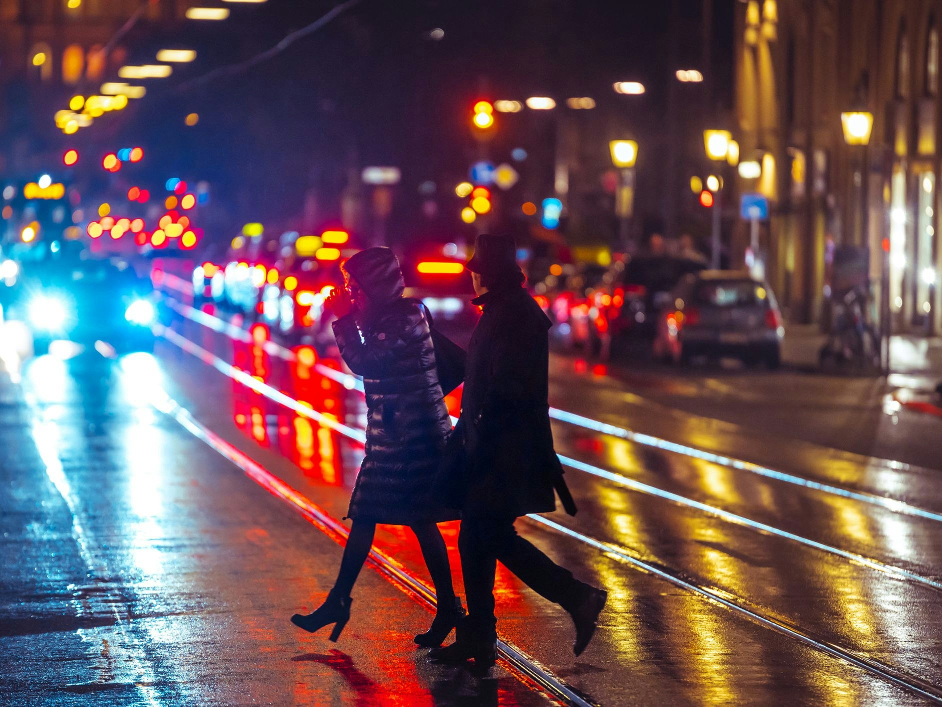 Munich, Germany – February 01, 2020: People crossing the street during a wet rainy night in Munich. Neon lights illuminating the scene. City traffic in the background.