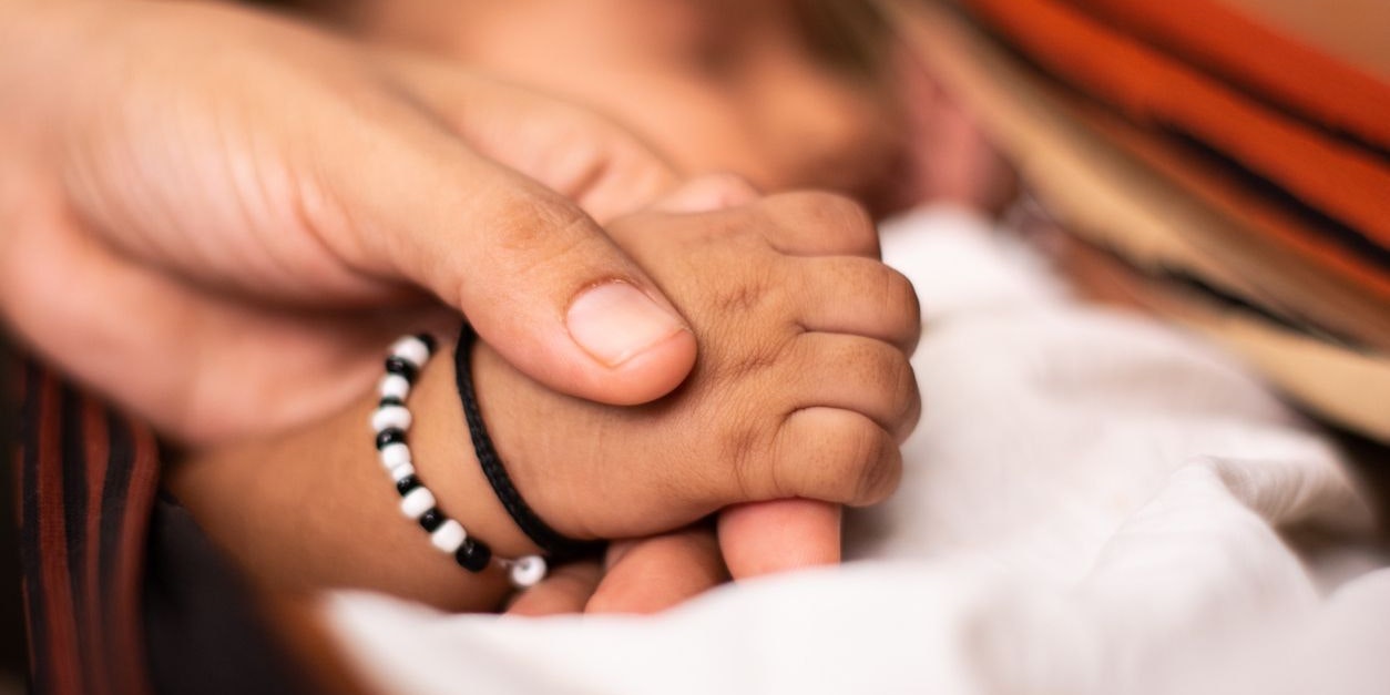 A newborn baby holding the parent hand while sleeping at cradle.