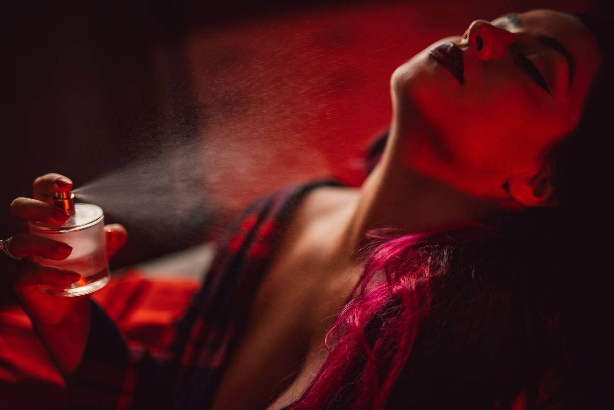 Beautiful young sedative plus size woman in a dress sitting putting on a perfume at home.
