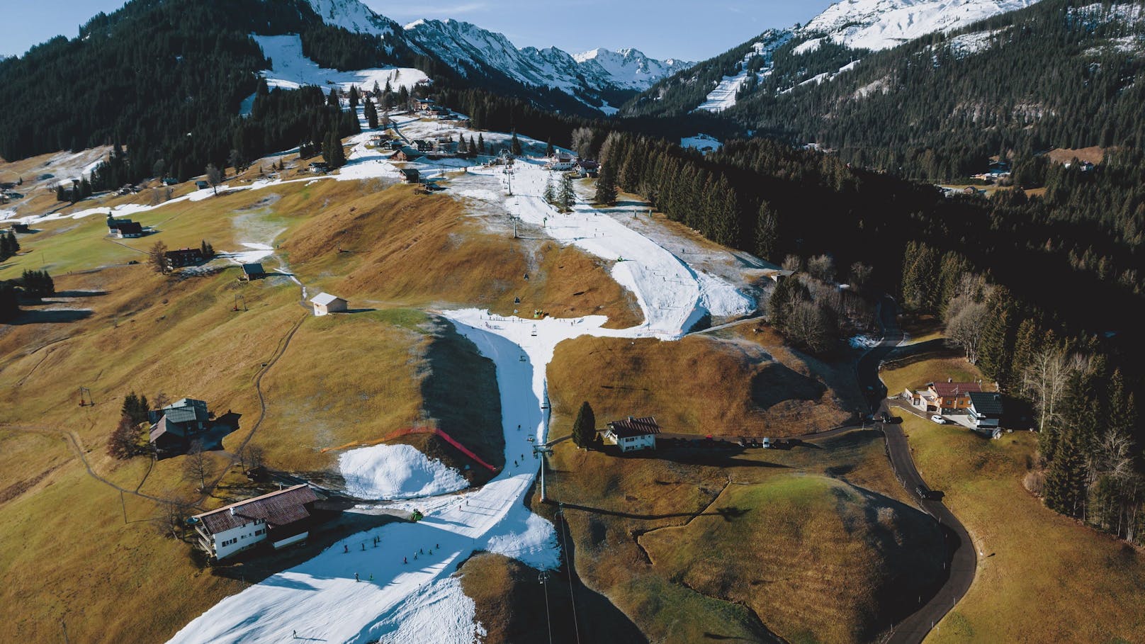 Schneeband einer Skipiste in der grünen Landschaft. Aufgrund des Warmwetters der letzten Tagen herrscht Schneemangel in den Skigebieten, aufgenommen am 30. Dezember 2022 in Riezlern, Österreich