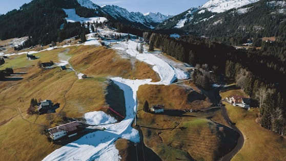 Schneeband einer Skipiste in der grünen Landschaft. Aufgrund des Warmwetters der letzten Tagen herrscht Schneemangel in den Skigebieten, aufgenommen am 30. Dezember 2022 in Riezlern, Österreich