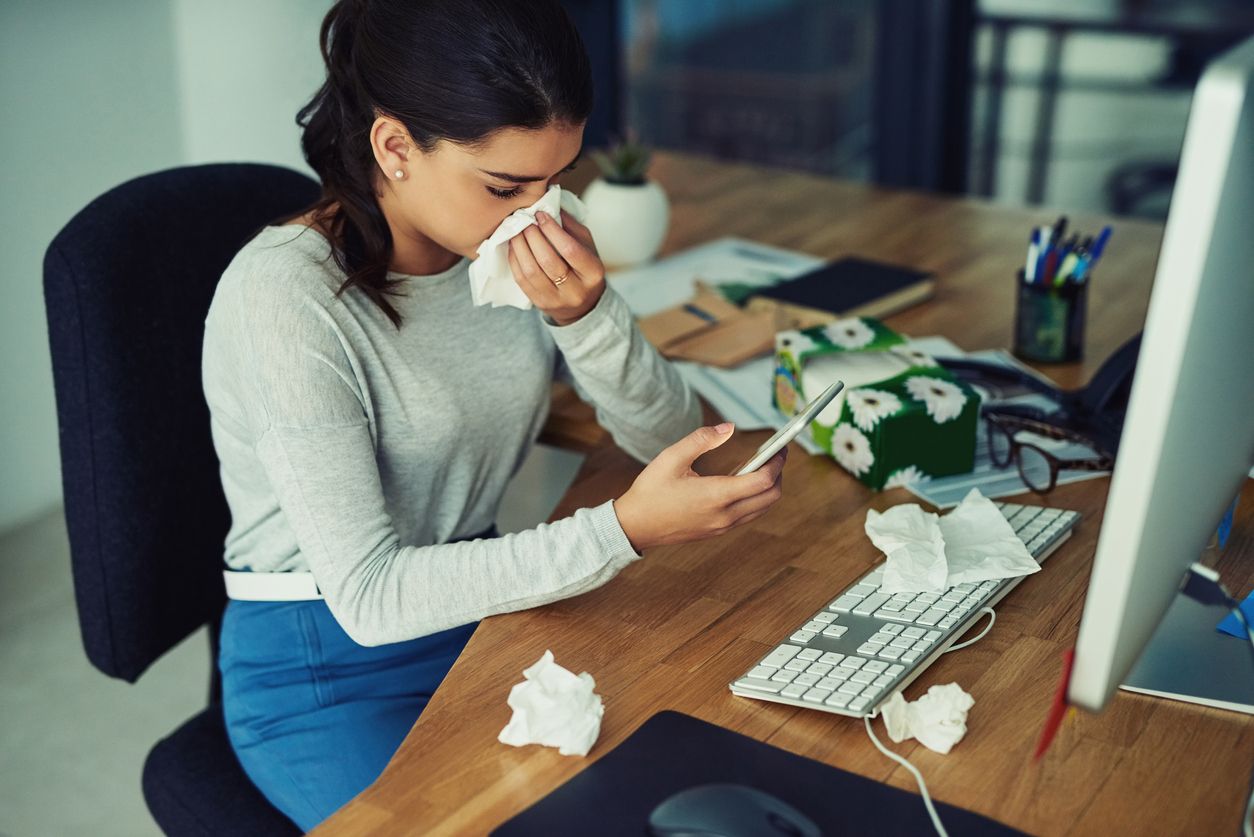 Shot of a young businesswoman blowing her nose while texting on a cellphone in an office
