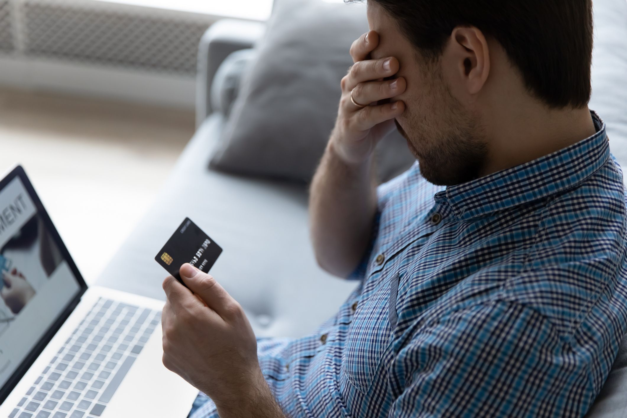 Close up unhappy man having problem with credit card, using laptop at home, depressed frustrated young customer client covering face with hand, loss money, cyber internet fraud and scam concept